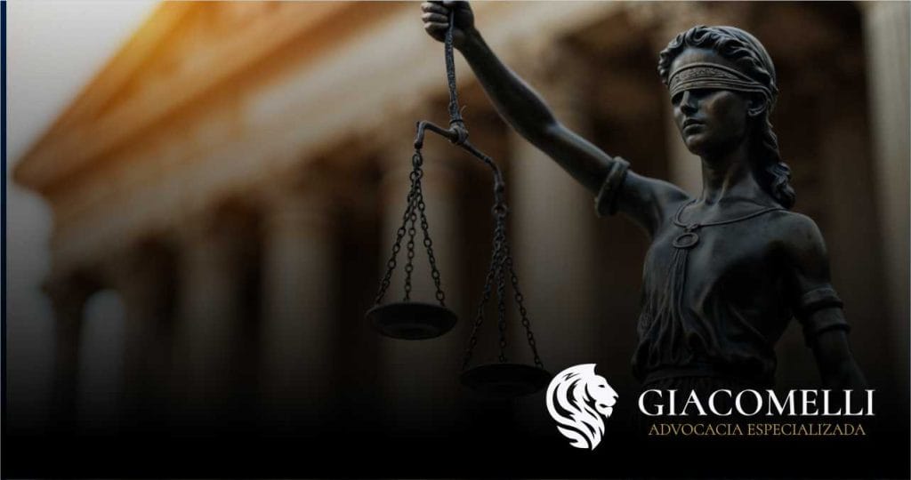 Estátua da Justiça em primeiro plano segurando uma balança, com colunas de um edifício judicial desfocadas ao fundo; logotipo da Giacomelli Advocacia no canto inferior direito.
